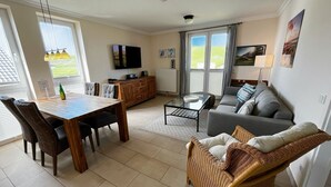 Uma sala de estar moderna com área de jantar, um sofá, uma poltrona de vime e uma televisão.