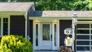 Une maison avec une porte d’entrée blanche, un garage portant le numéro 62, et une pile de bois de chauffage à l’extérieur.