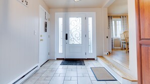 Un couloir propre et bien éclairé, avec une porte blanche ornée d’un panneau de verre décoratif, un sol carrelé et un banc en bois à l’arrière-plan.
