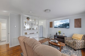 A living room with a beige sofa, patterned armchair, and a flat-screen TV mounted on the wall.