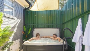 Een jacuzzi met twee personen, omringd door een groene hekken en een witte muur.