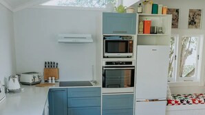 Kompakti keittiö, jossa on siniset kaapit, mikroaaltouuni, leivänpaahdin ja pieni jääkaappi.