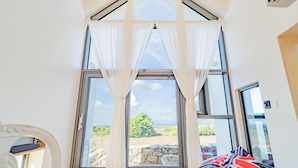 A room with a large window, white curtains, a bean bag, and a view of the outdoors. - Jeju Geunalohu Pension (Jeju City)