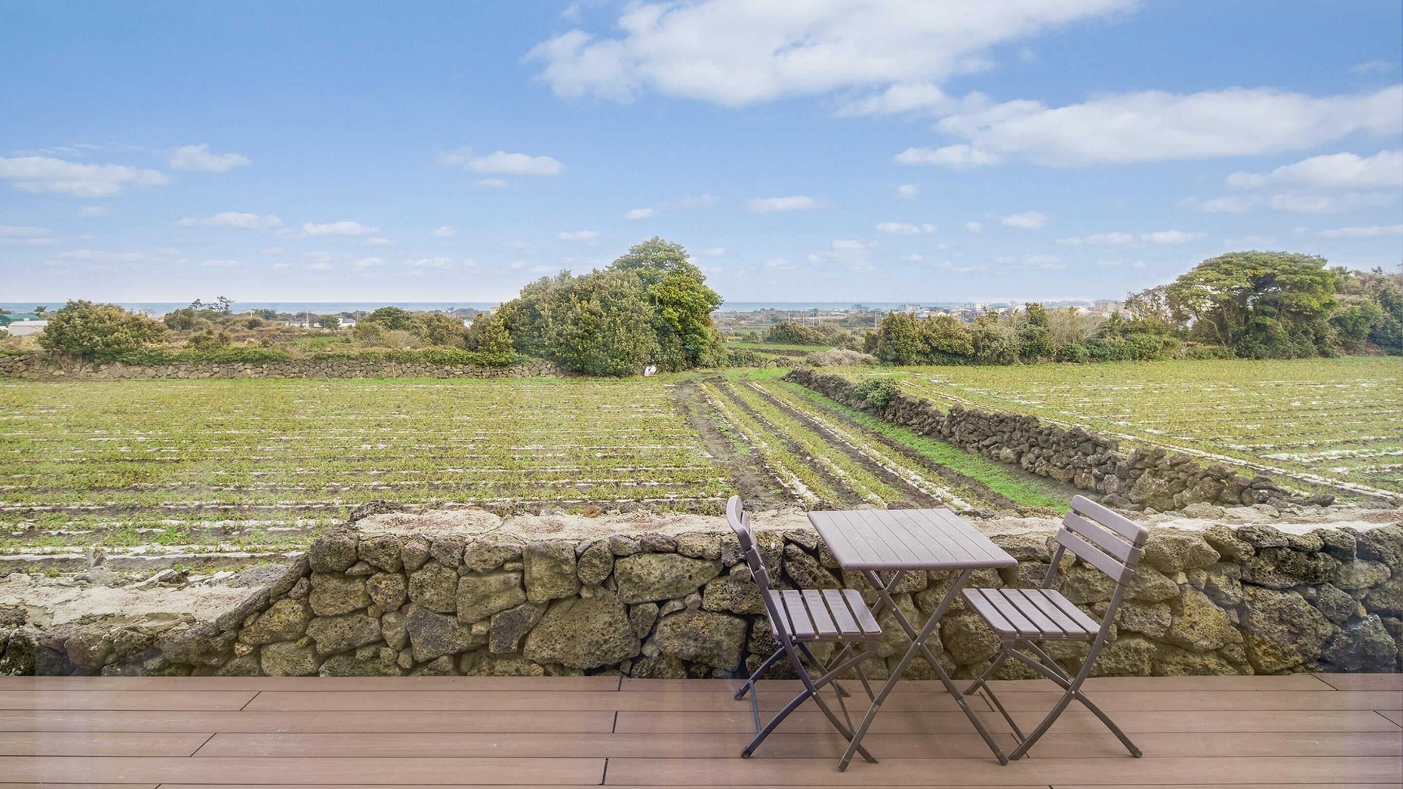 Una terraza con muro de piedra, cubierta de madera y vista a campos de cultivo.