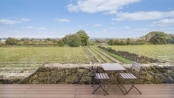 A terrace with a stone wall, wooden deck, and a view of agricultural fields.