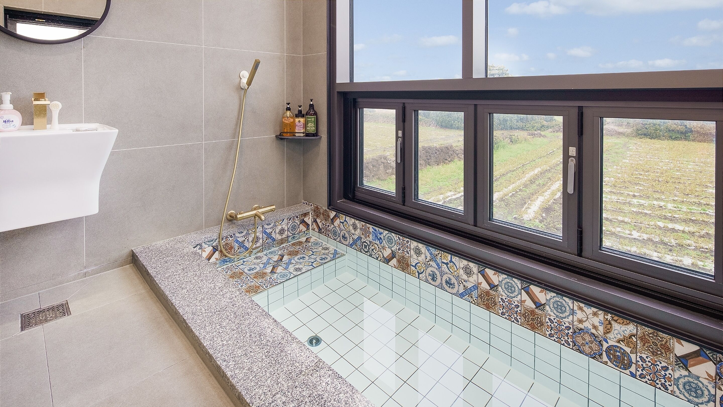 Ein Badezimmer mit großem Fenster, einer Dusche mit goldfarbenem Wasserhahn und einem gefliesten Boden.