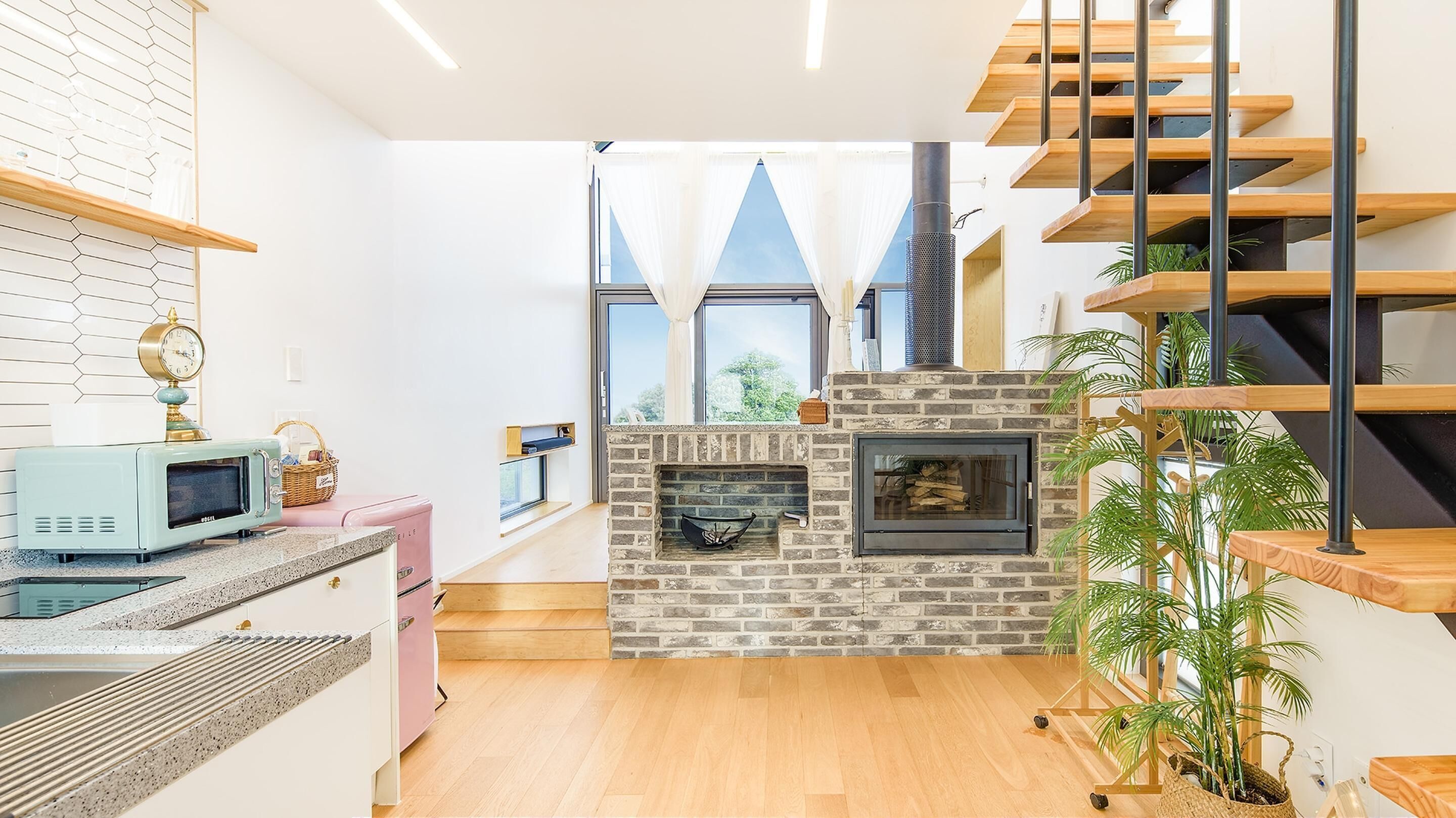 Una cocina moderna con chimenea de ladrillo, escalera de madera y ventanas amplias.