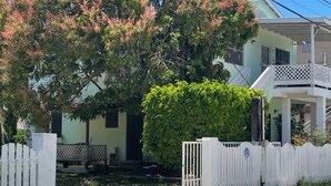 Un barrio residencial con una casa, cerca blanca y un árbol con flores rosadas.