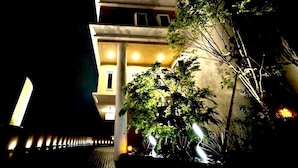 Um edifício à noite, com janelas iluminadas e uma árvore em primeiro plano.