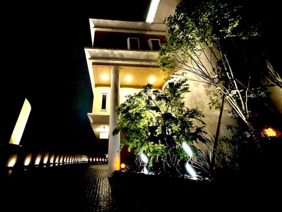 A building at night with illuminated windows and a tree in the foreground.