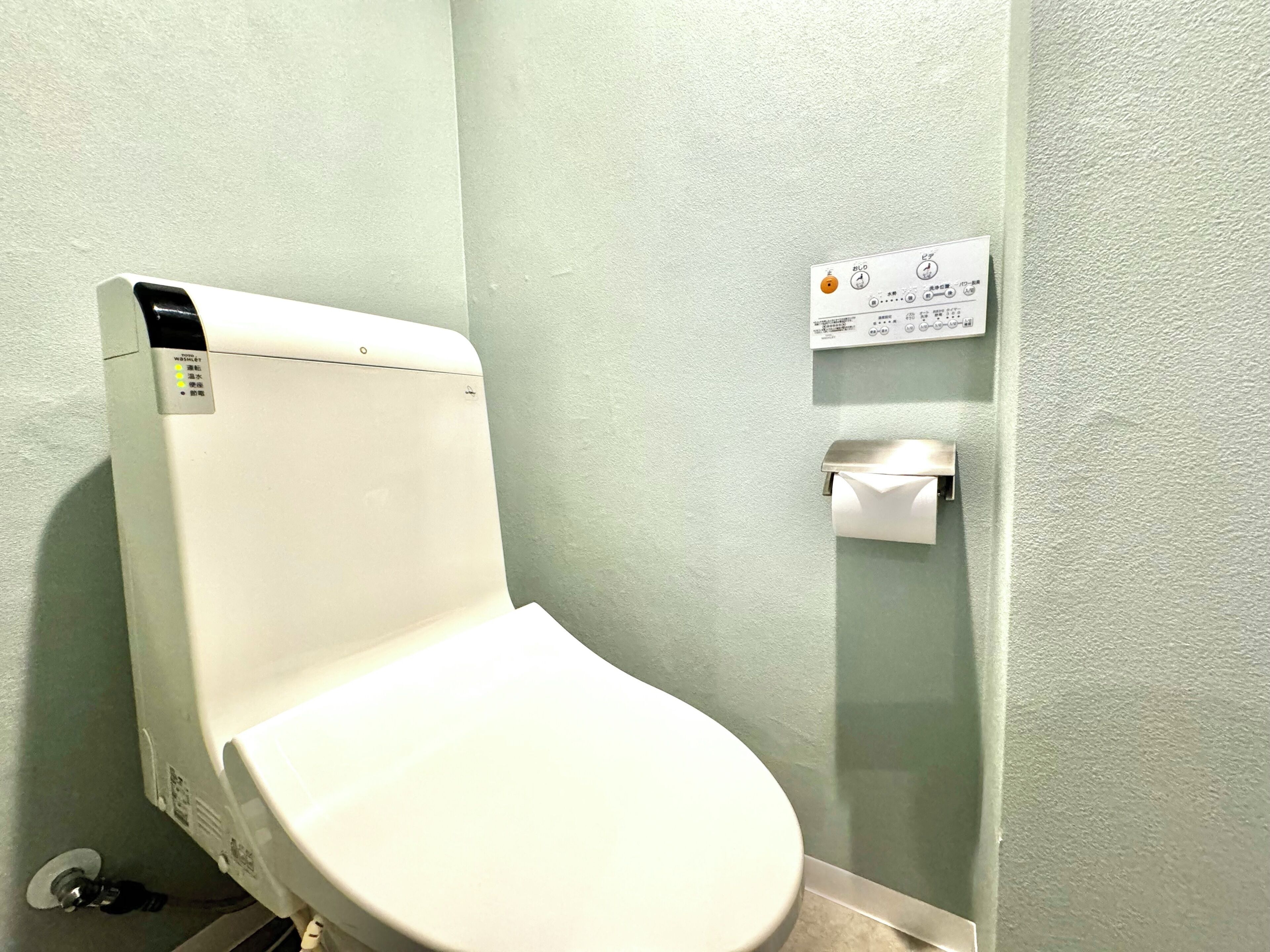 A white toilet with a control panel and a toilet paper holder on the wall.