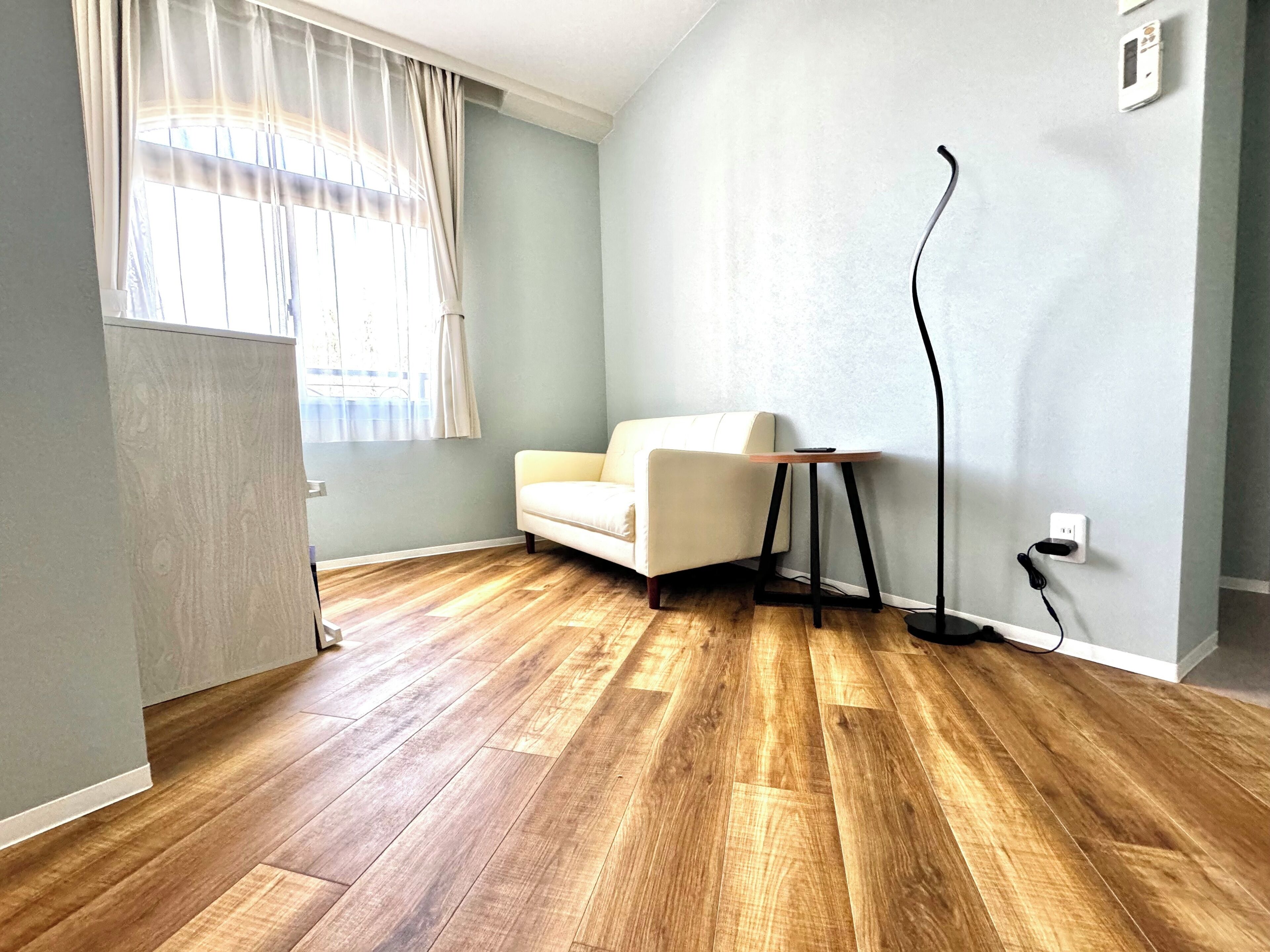 Ein Zimmer mit Holzboden, einem weißen Sofa, einem kleinen Tisch und einer Stehlampe.
