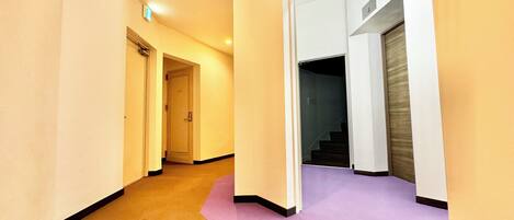 Un pasillo con pisos alfombrados, una puerta que da a una escalera y un detector de incendios visible en el techo.