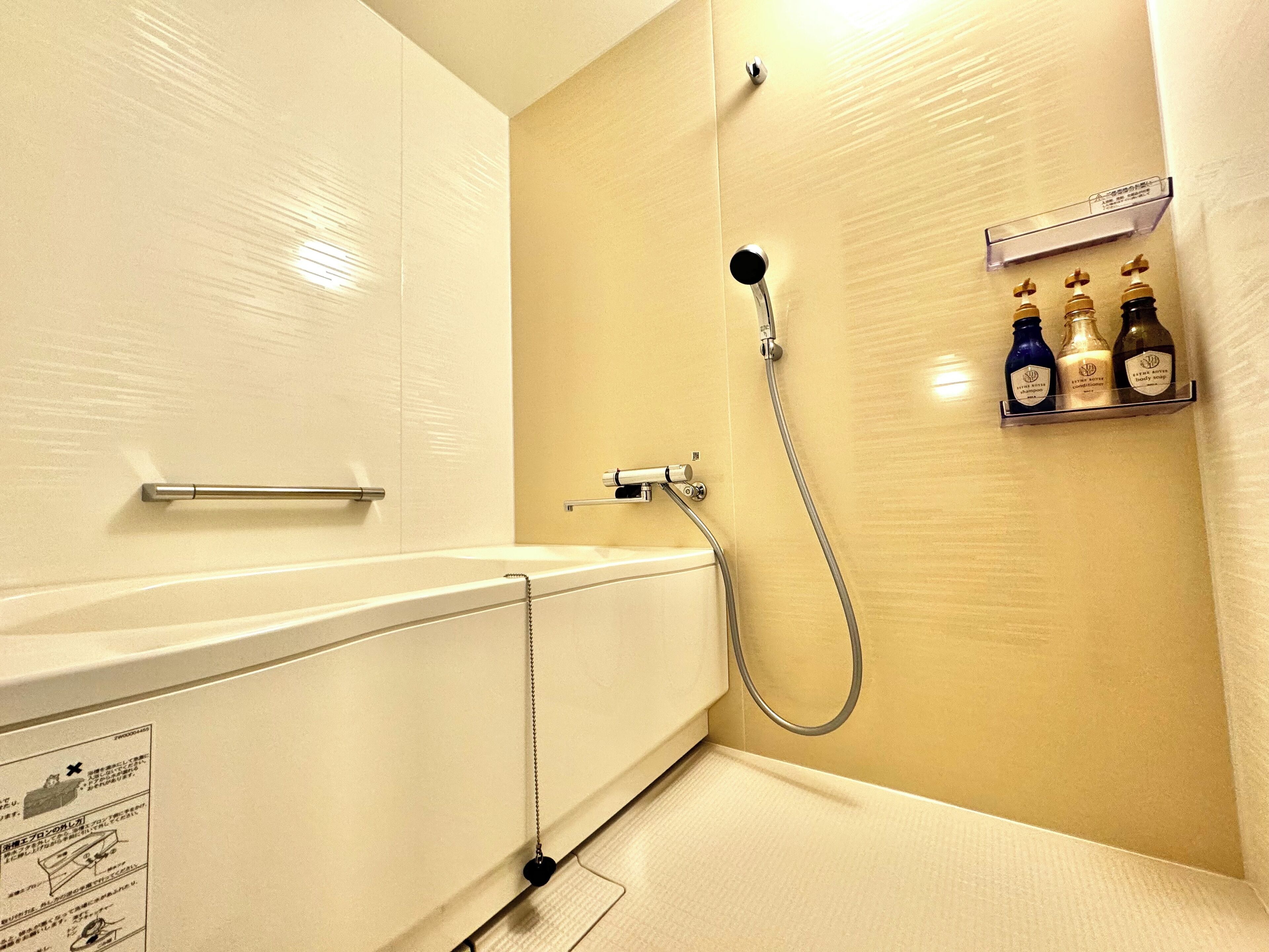 A bathroom with a bathtub, a shower, and a shelf with three bottles of toiletries.