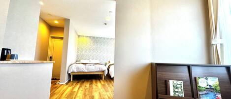 Habitación de hotel con piso de madera, cama, escritorio pequeño y aire acondicionado instalado en la pared.
