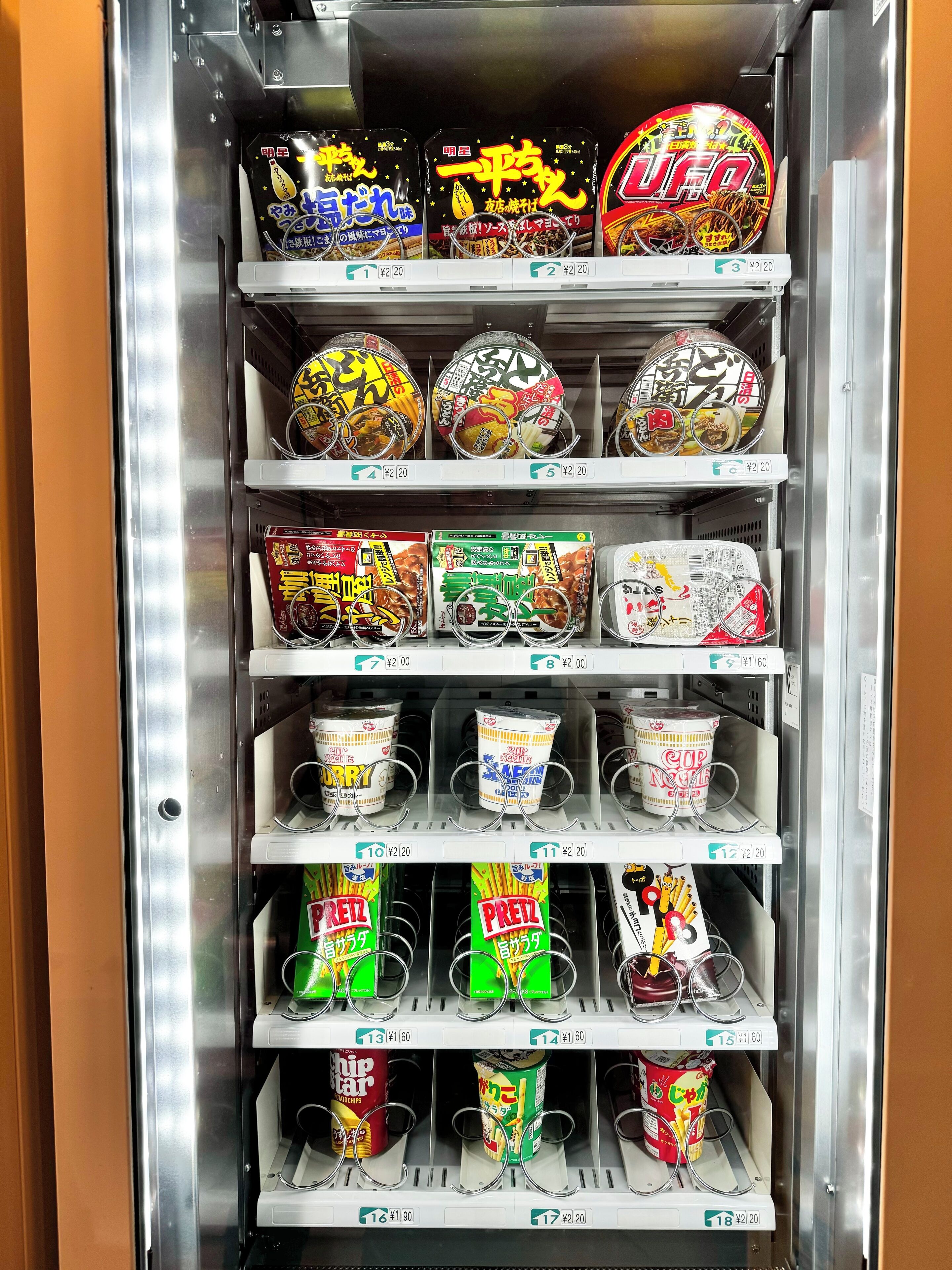 A vending machine stocked with various food items including instant noodles, cups, and snacks.