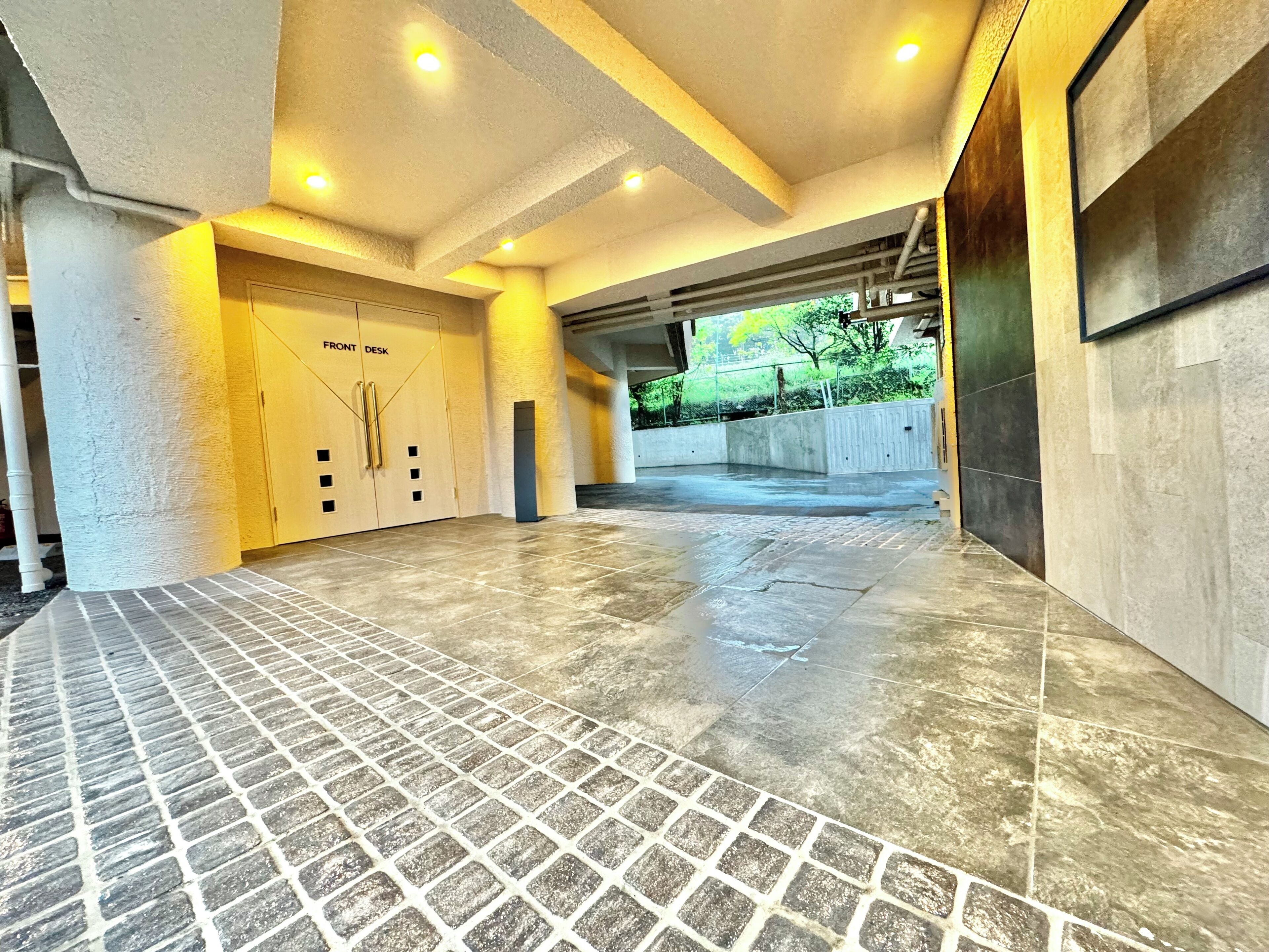 A spacious lobby with a tiled floor, a front desk area, and a view of greenery outside.
