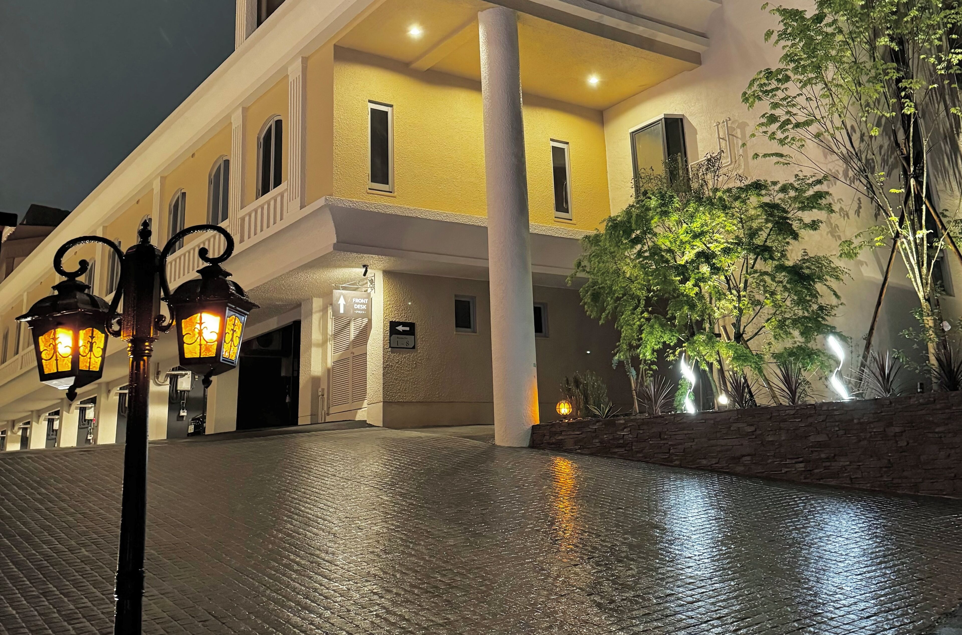 A hotel entrance with a paved walkway, a sign indicating the front desk, and a large column.