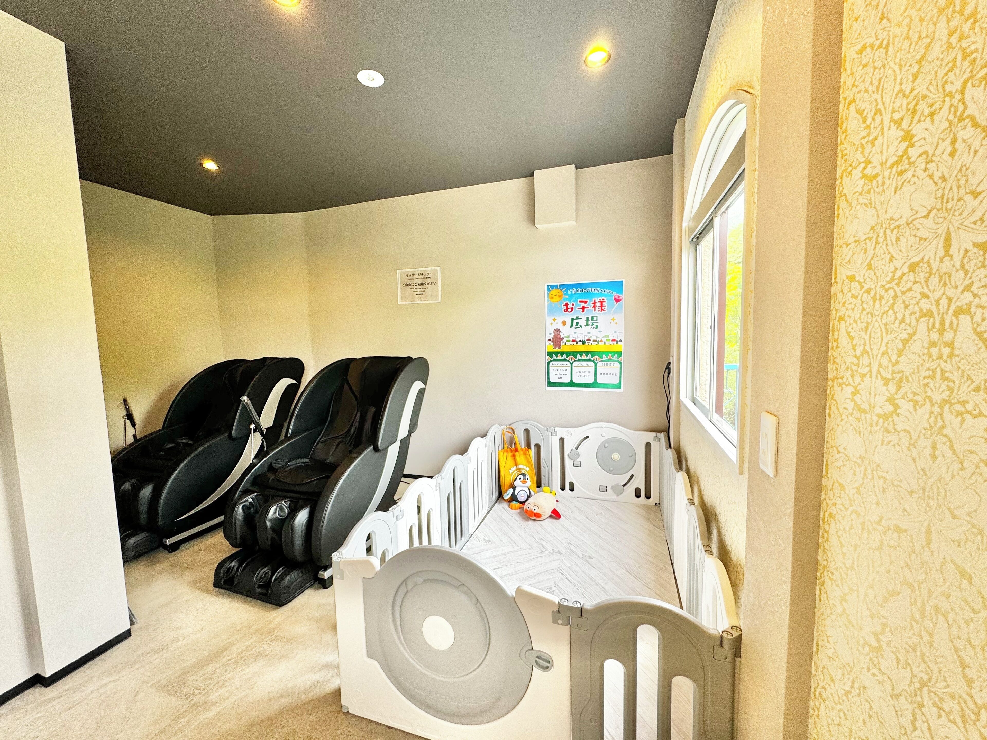 A room with two massage chairs, a small bed with a toy, and a window with a view.