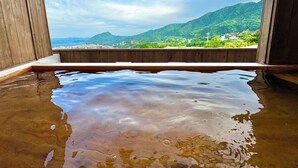 Banho em águas termais com borda de madeira e vista para a cidade e montanhas ao fundo.