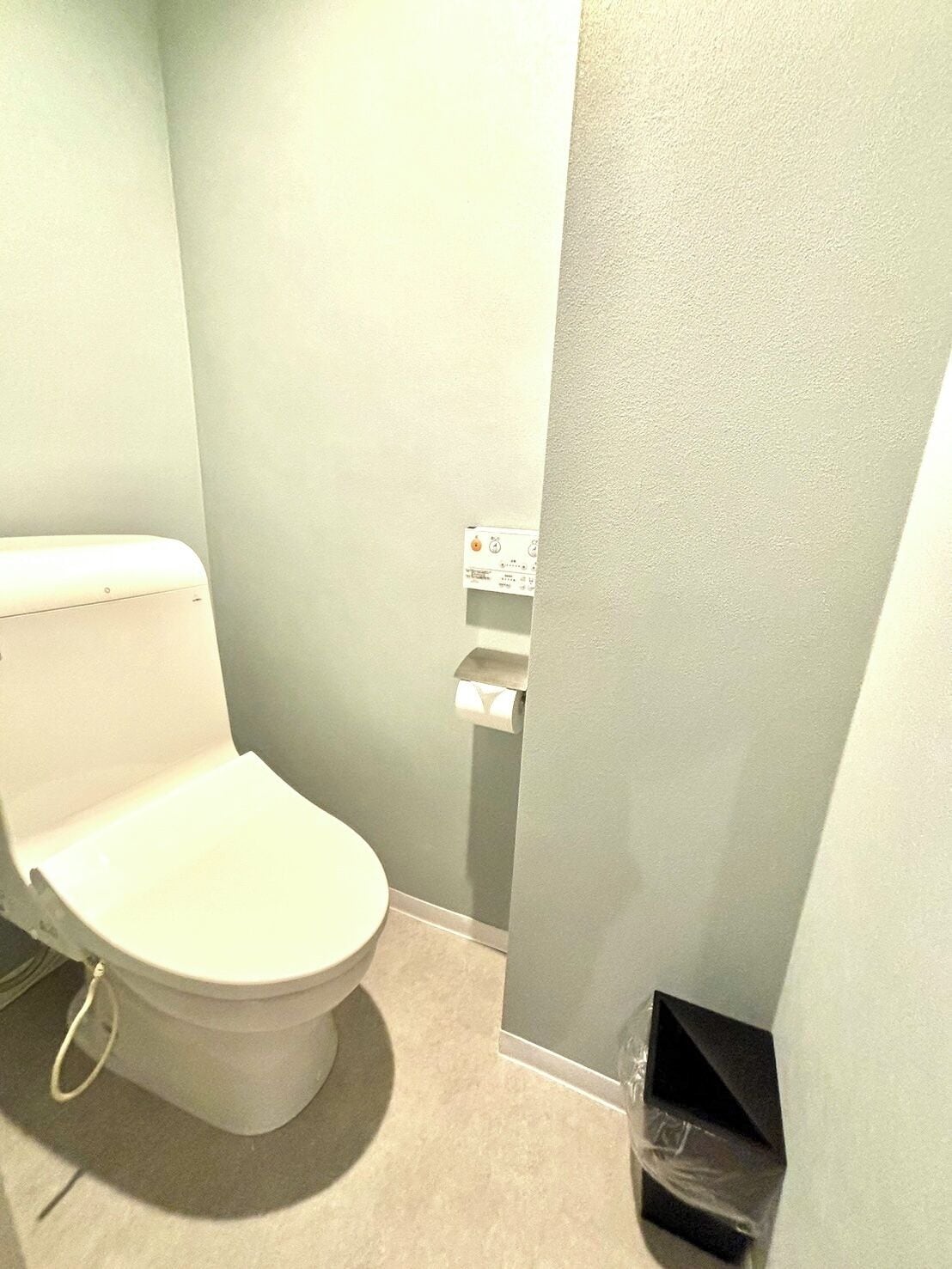 Casa de banho pequena e compacta com sanita, autoclismo embutido na parede e um cesto de lixo.