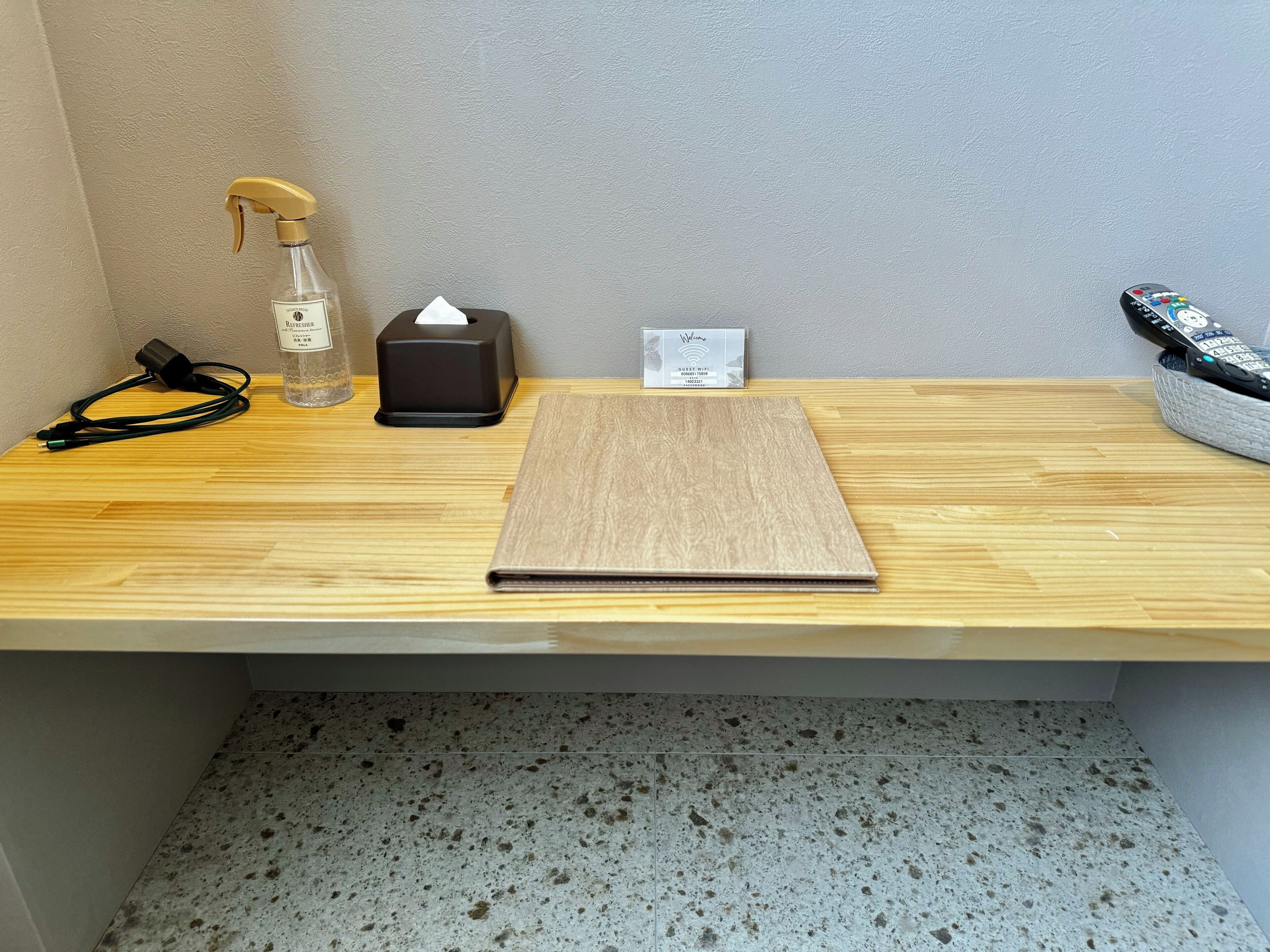 Un escritorio de madera con una caja de pañuelos, un atomizador, un control remoto y una regleta.