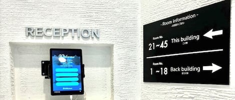 A reception area with a digital screen displaying a welcome message, a sign indicating room numbers 21-45 and 1-18, and a directional sign for the back building.