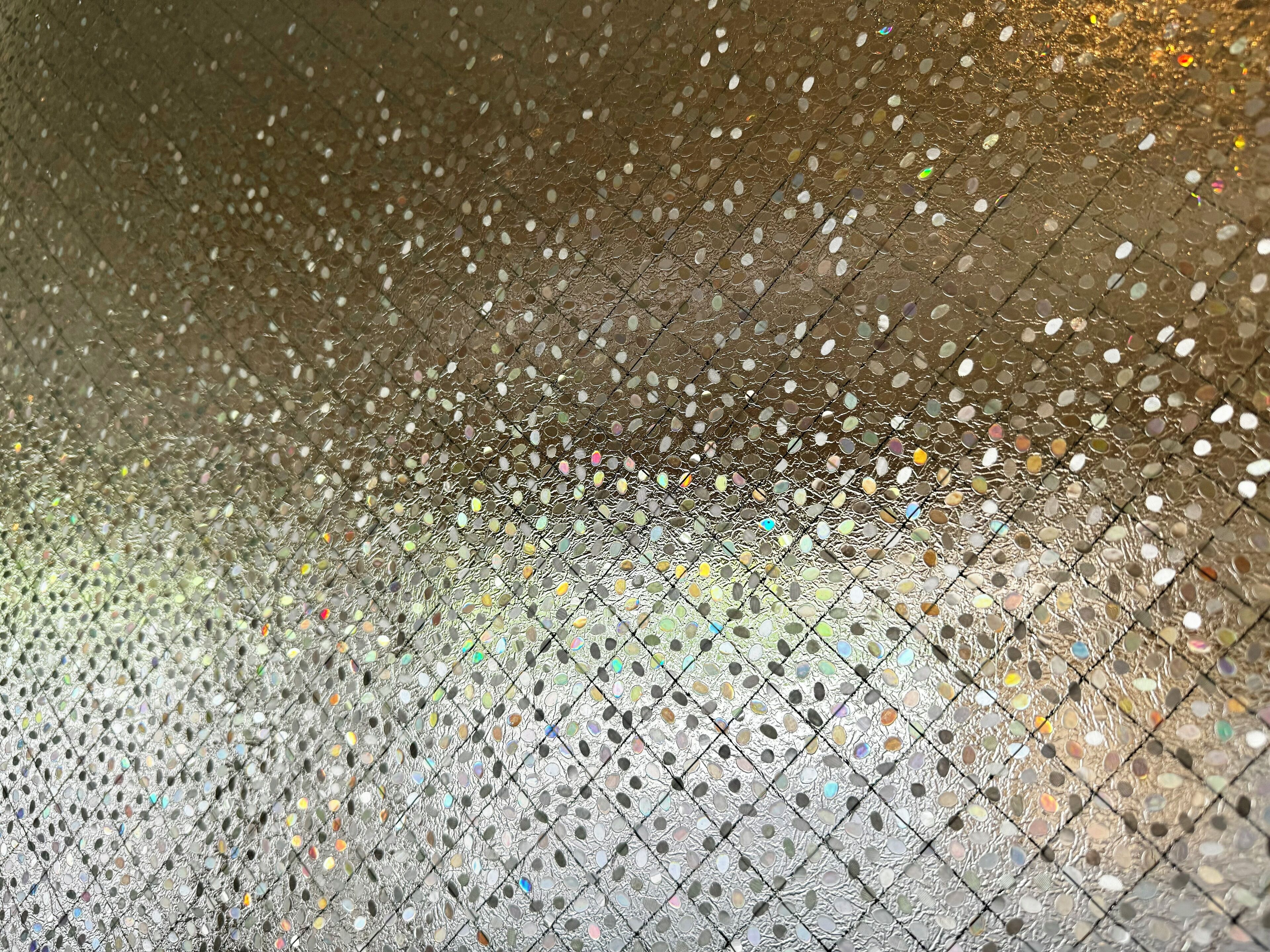 A close-up of a textured surface with a pattern of small, reflective, multicolored elements.