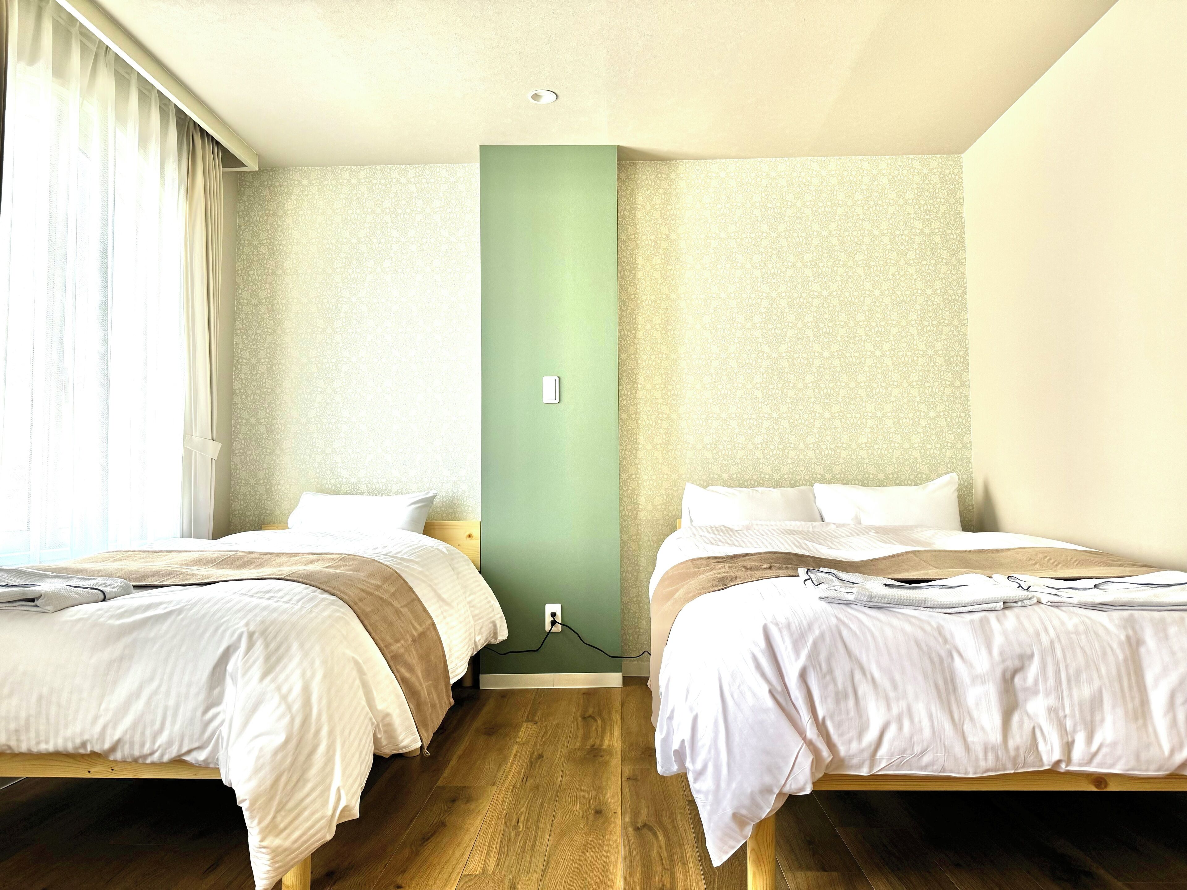 A hotel room with two beds, a green accent wall, and wooden flooring.