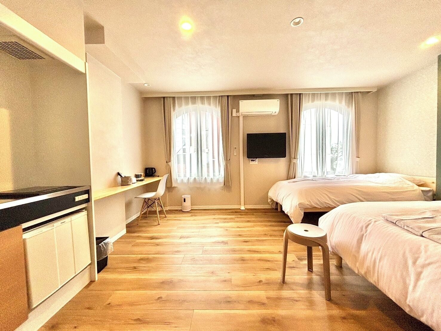 A hotel room with a wooden floor, a desk with a chair, a bed, and a TV mounted on the wall.