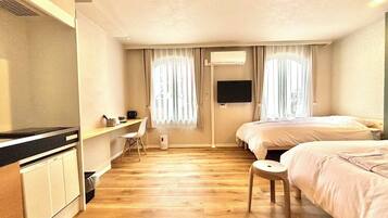 A hotel room with a wooden floor, a desk with a chair, a bed, and a TV mounted on the wall.