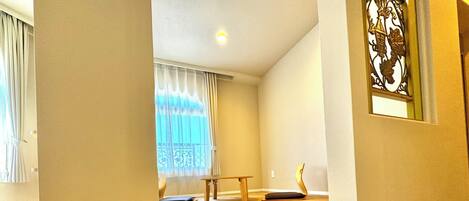 Una habitación con suelo de madera, una mesita, un banco y una ventana con cortinas.