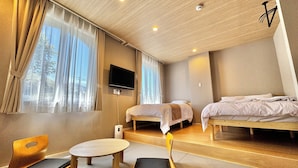 Quarto de hotel moderno com duas camas, televisão, uma mesa pequena e uma cadeira.