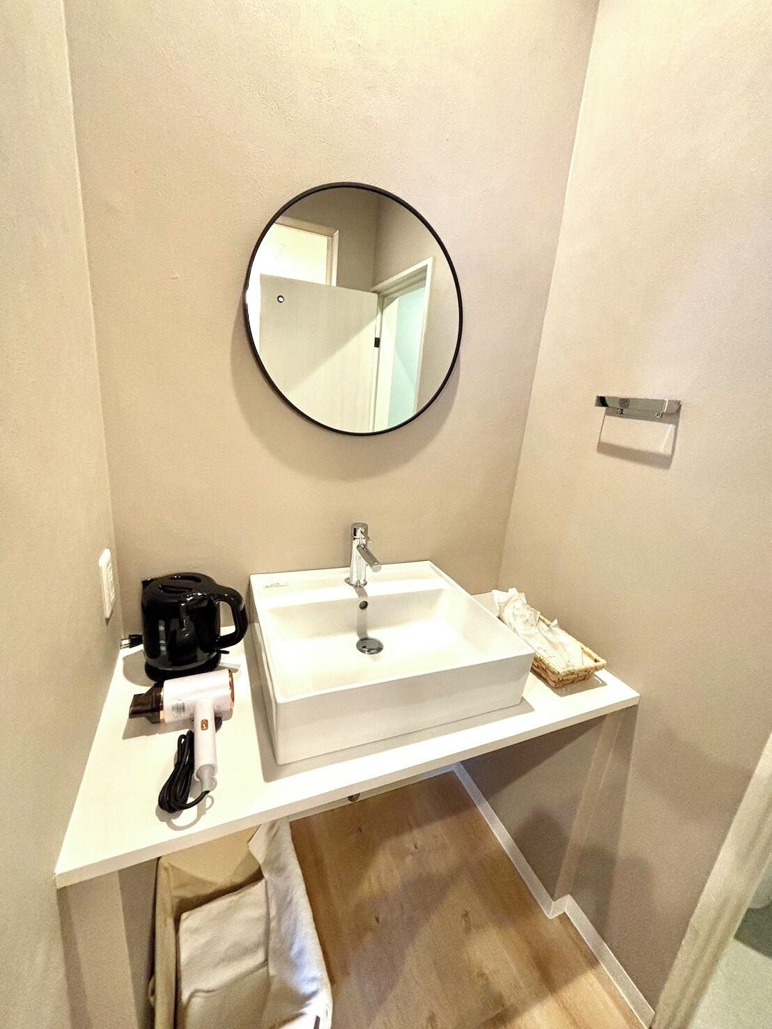 A small bathroom with a white sink, a round mirror, and a black coffee maker.