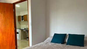 A bedroom with a bed, two pillows, and a wooden door leading to a kitchen area.