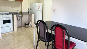 A kitchen with a stove, sink, and refrigerator, and a dining table with chairs.