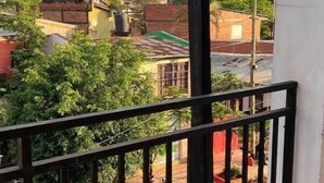 A balcony with a metal railing overlooking a residential area with houses and greenery.