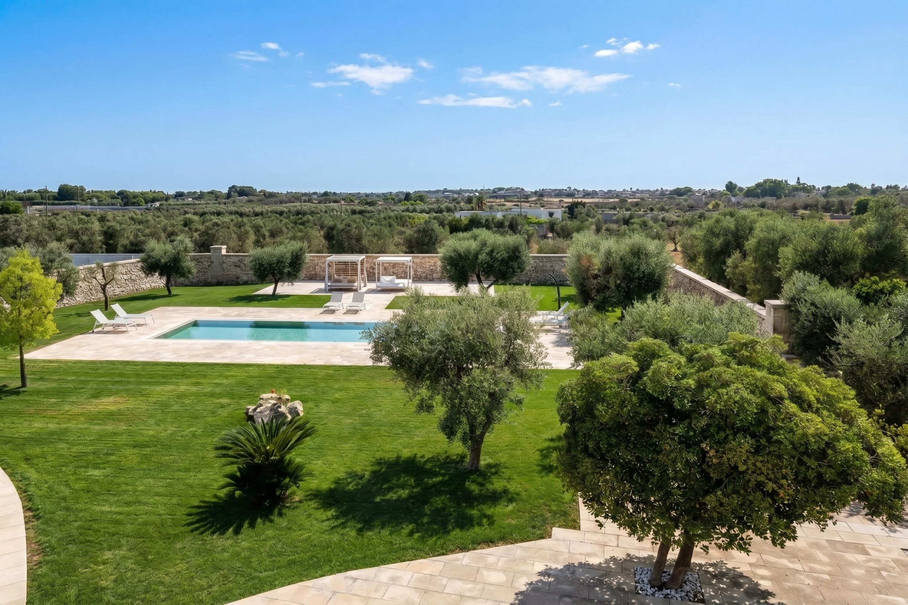 A landscaped outdoor area with a swimming pool, stone walls, and various trees.