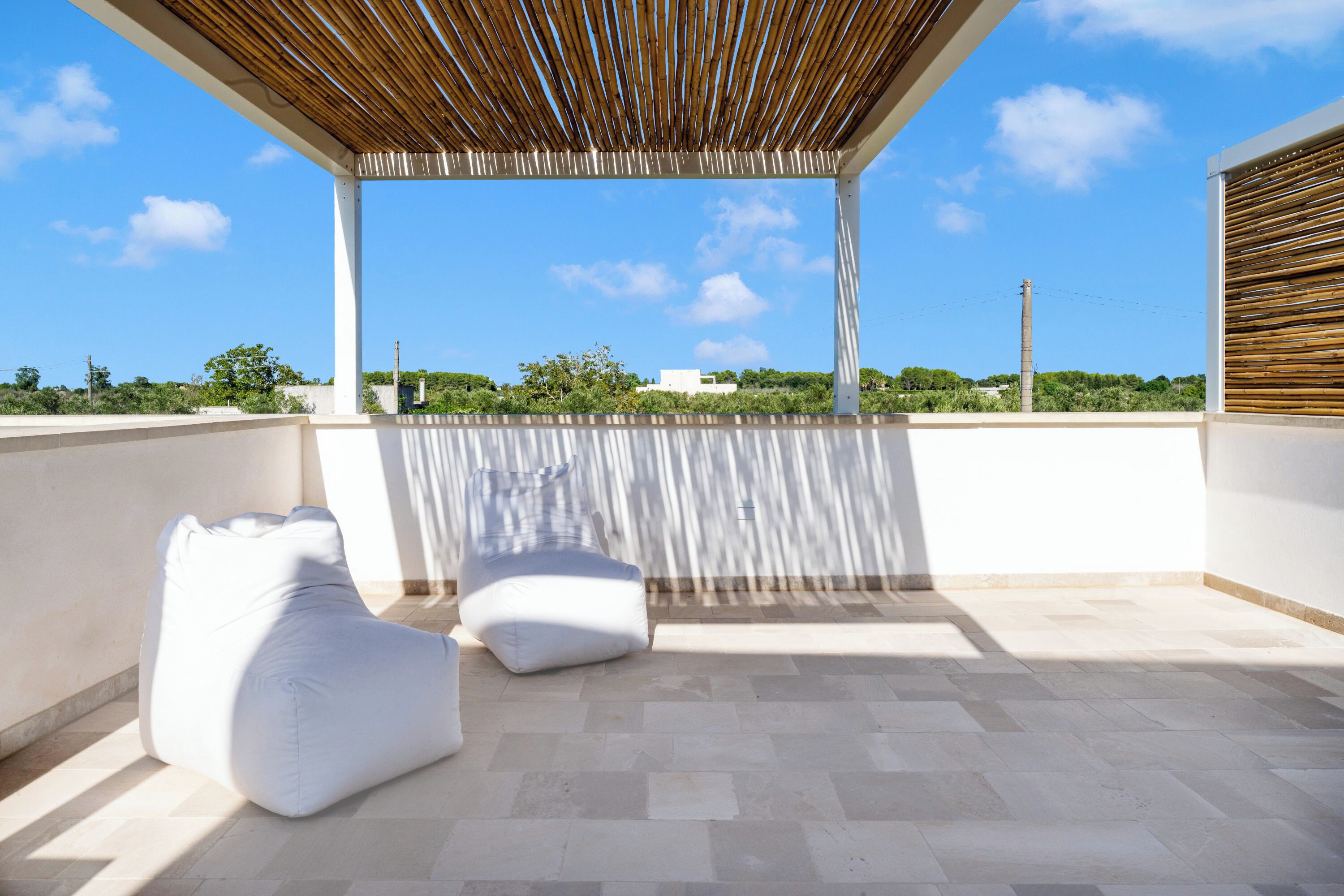 A covered outdoor seating area with two white bean bags, a wooden ceiling, and a view of the sky and greenery.