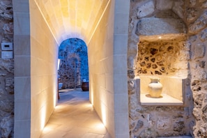 A stone corridor with a tiled floor, a stone wall with a shelf, and a blue-tiled archway.
