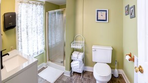 Un bagno con doccia, WC, lavandino e un piccolo ripiano bianco con asciugamani.