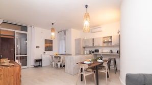 A modern kitchen with a dining area, featuring a wooden table, white chairs, and pendant lighting. - Secret Garden House, Portisco, Italy (Portisco)