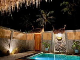 Zona junto a la piscina con una puerta de madera, un muro de piedra y una estructura de techo de paja.