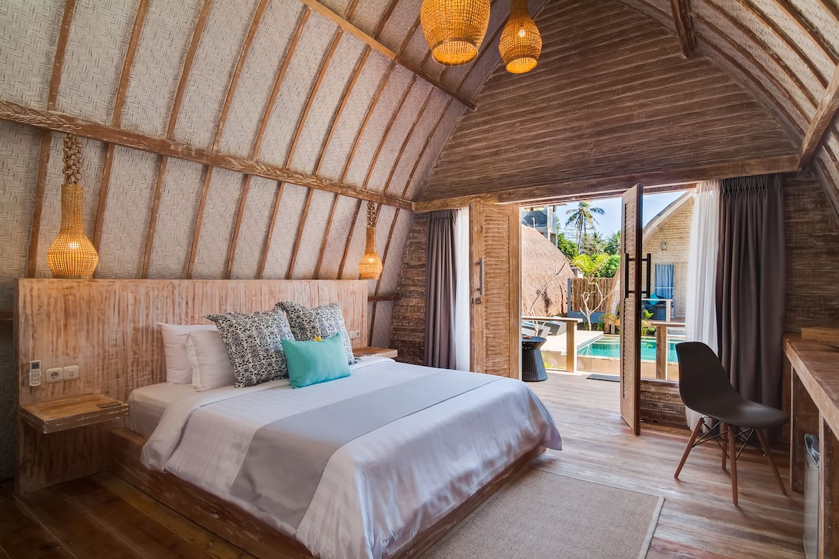A bedroom with a large bed, wooden ceiling, and a view of a pool and outdoor area.