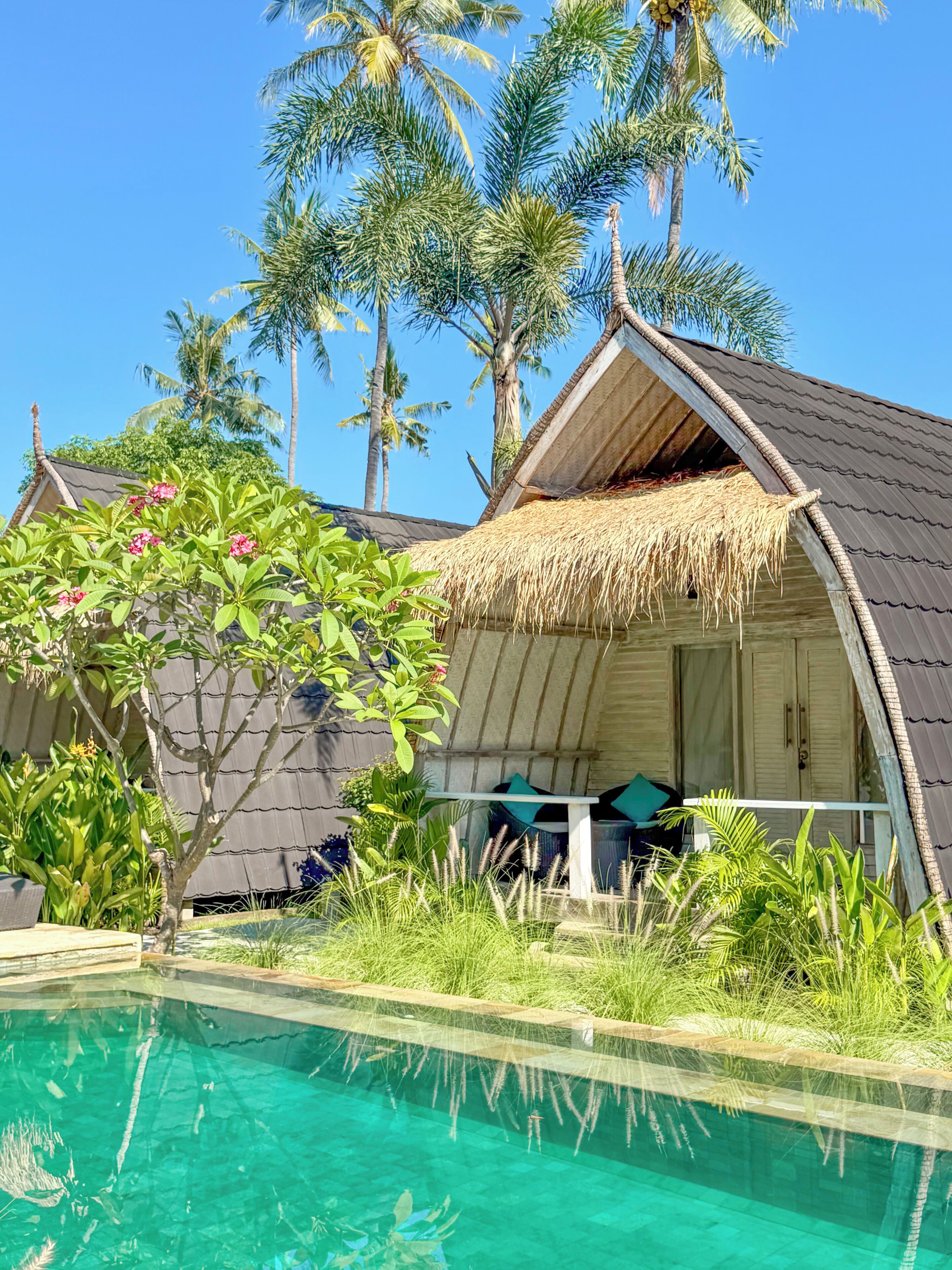 A poolside view of a resort with overwater bungalows, clear blue pool, and lush tropical vegetation.