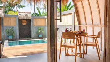 Area piscina con veranda in legno, tavolo e sedie, e piante in vaso.