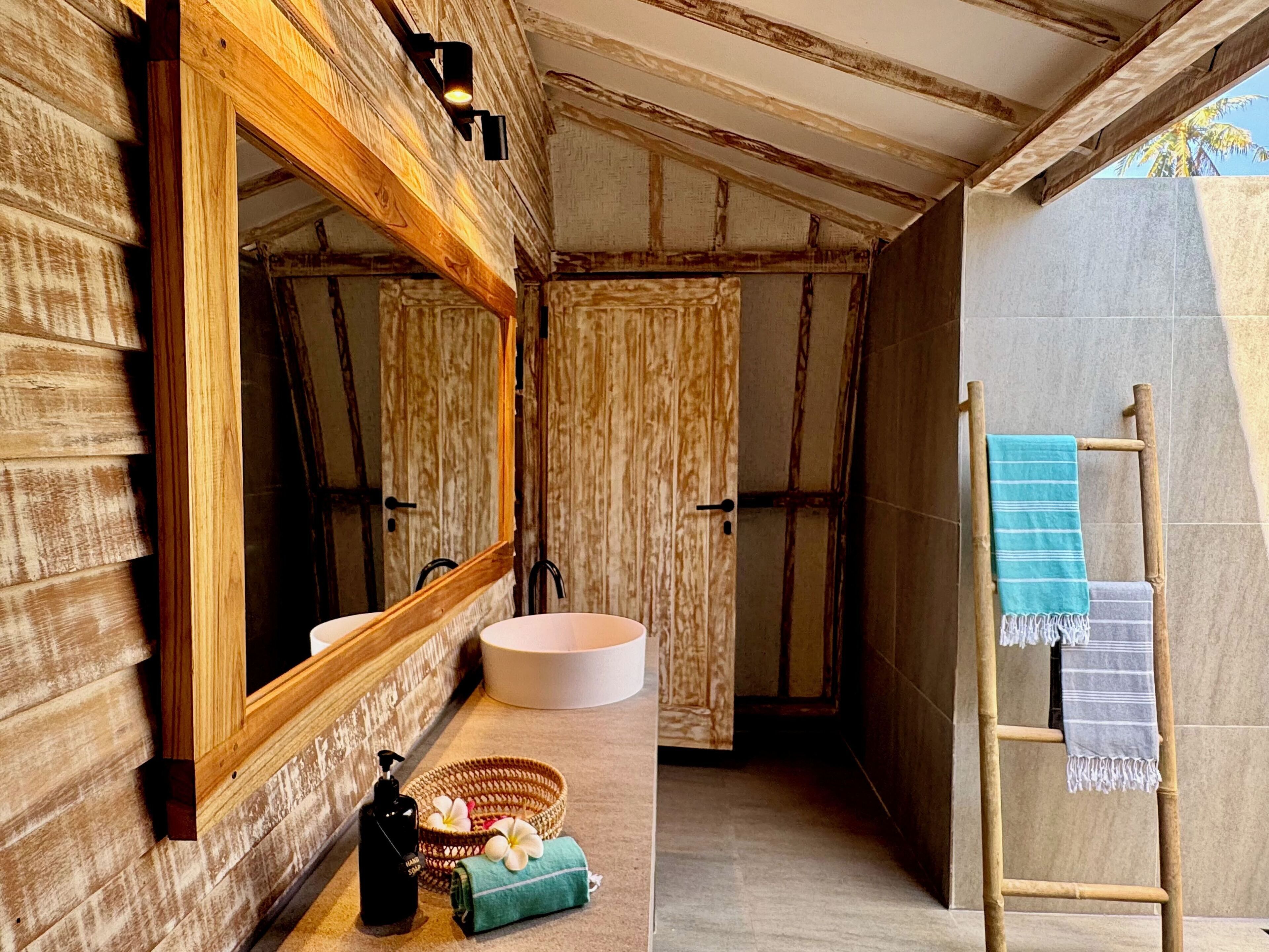 A bathroom with a wooden exterior, a large mirror, a round sink, and a wooden ladder with towels.