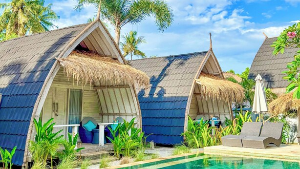 Een resort met bungalows boven het water, een zwembad en tropische begroeiing.