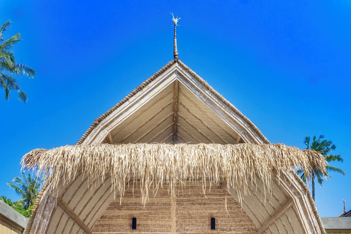 A thatched-roof structure with a pool, lounge chairs, and a view of the sky.