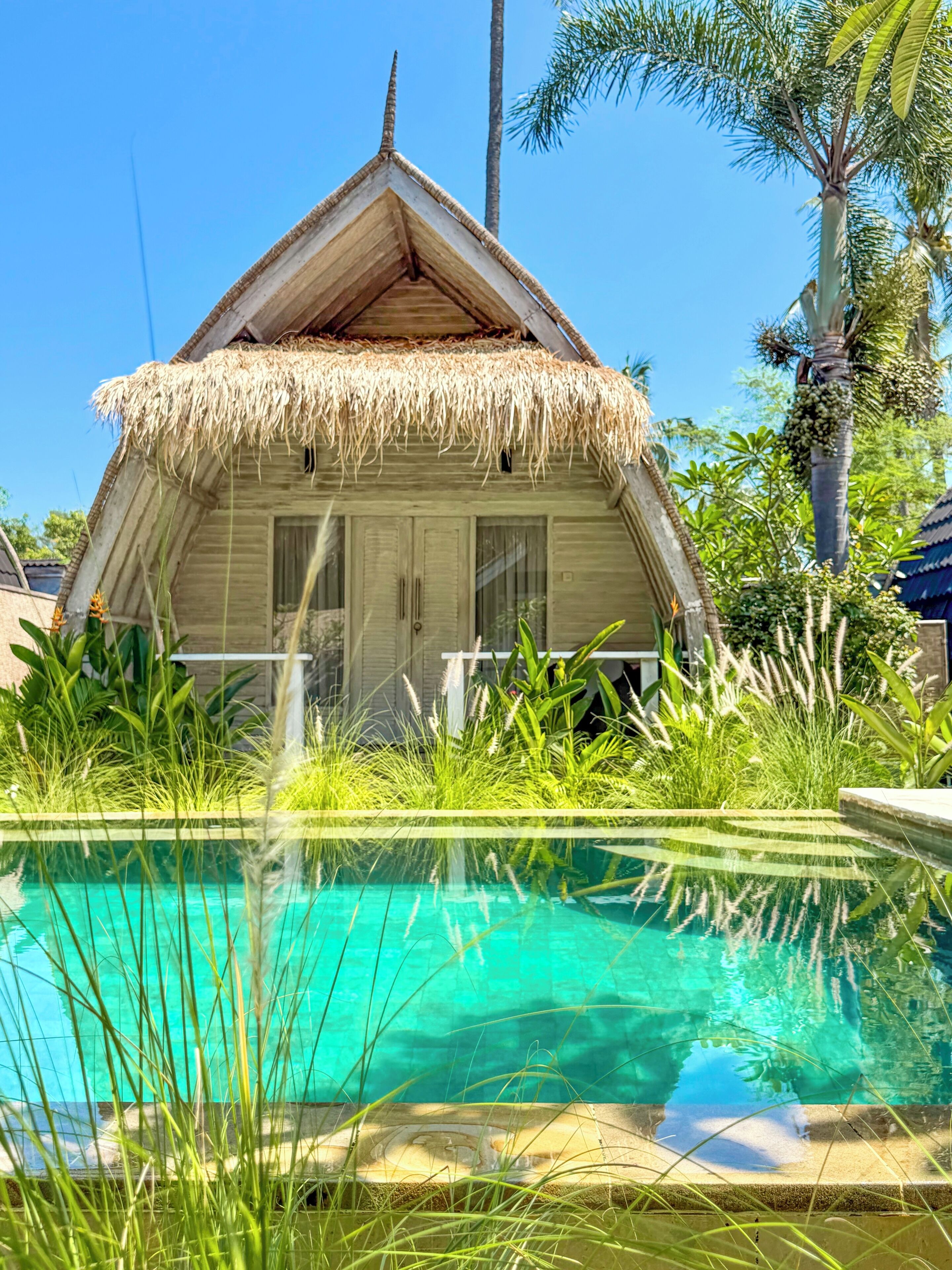Un bungalow au toit de chaume avec une piscine devant.
